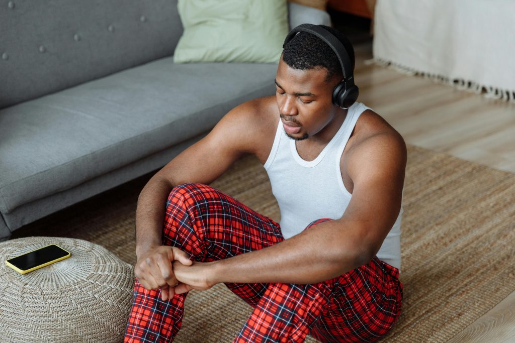 African American man in headphones relaxing on floor with phone nearby indoors.